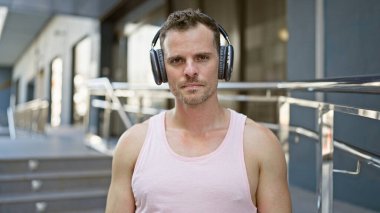 Kulaklıklı yakışıklı bir adam, şehir sokaklarında kendine güvenen bir şekilde dikiliyor..