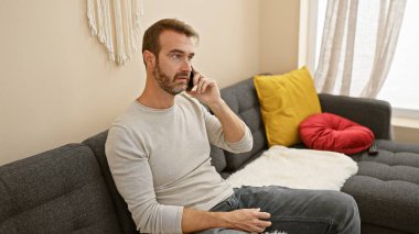 Samimi bir oturma odasında, telefonda konuşan orta yaşlı İspanyol bir adam. Kapalı mekâna kişisel bir dokunuş eklemiş..