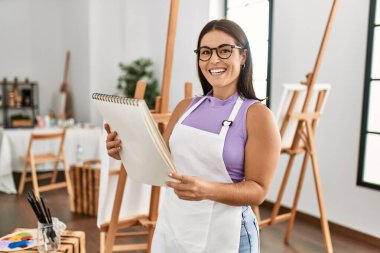 Young beautiful hispanic woman artist smiling confident looking draw on notebook at art studio