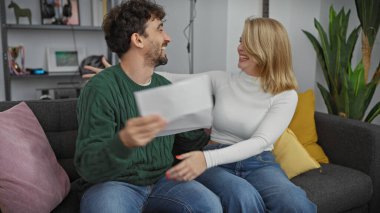 Gülen çift rahat bir oturma odasında evrak paylaşıyor, samimiyet ve aile hayatı sergiliyor..