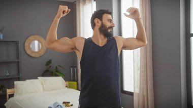 Sakallı bir adam modern bir yatak odasında kaslarını rahatça esnetir. Fitness ve sağlıklı bir yaşam tarzını teşvik eder..