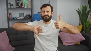 Sakallı adam modern bir oturma odasında baş parmağını sallayarak hareket ettiriyor.
