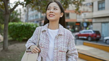 Güzel, genç Asyalı bir kadın yeşil doğayla kaplı bir cadde boyunca mutlu bir şekilde yürüyor..
