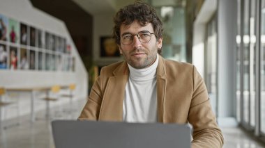 Ofiste dizüstü bilgisayar kullanarak gözlük takan sakallı yakışıklı bir İspanyol.