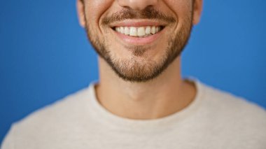 Işıldayan, sakallı, genç bir İspanyol adam canlı, mavi bir arka plana karşı poz veriyor..