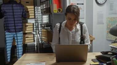 Polis departmanında dizüstü bilgisayarda çalışan kadın ajan, arka plandaki adam, soruşturma kurulu görünür..