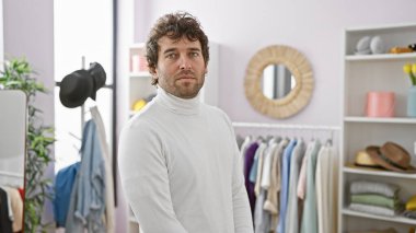 Beyaz balıkçı yakalı, sakallı yakışıklı genç adam modern bir giyim odasında moda ve tarz aktarıyor..