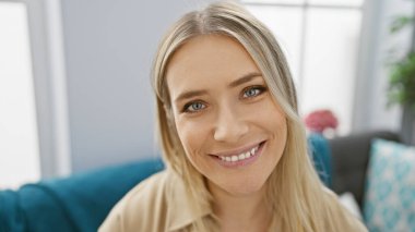 Kendine güveni tam genç bir sarışının rahatlamanın tadını çıkarması, gülümsemesi ve evdeki rahat koltukta oturması.