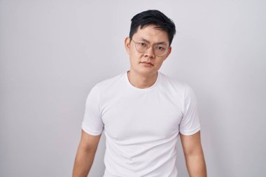 Beyaz arka planda duran Asyalı genç adam uykulu ve yorgun görünüyor, yorgunluktan yorgun ve akşamdan kalma, sabahları tembel gözler.. 