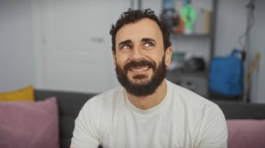 Gülümseyen sakallı bir adamın modern bir oturma odasında rahat bir şekilde uzanırken rahat bir rahatlama sergiliyor..