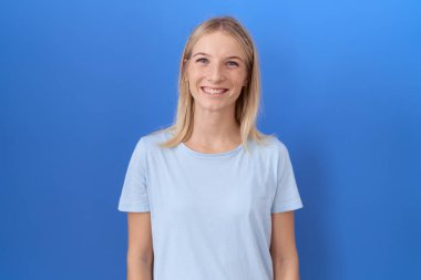 Yüzünde mutlu ve havalı bir gülümseme olan günlük mavi tişört giyen beyaz bir kadın. şanslı kişi. 