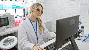 Modern laboratuvarda bilgisayar üzerinde çalışan genç sarışın kadın bilim adamı.