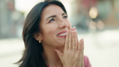 Middle age hispanic woman praying with closed eyes at street