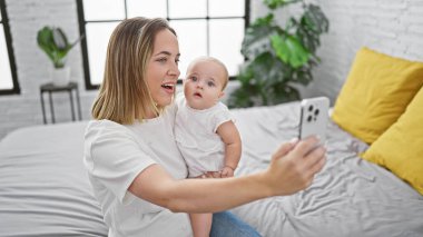 Mutlu anne ve kız özgüvenli selfie çekiyorlar ve rahat odada birlikte geçirdikleri değerli anları yakalıyorlar. Yatakta oturuyorlar, akıllı telefonlar kullanıyorlar, günlük yaşam tarzları..