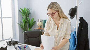 Profesyonel sarışın bir kadın modern bir ofiste belgeleri inceliyor, iş, odaklanma ve organizasyonu somutlaştırıyor..