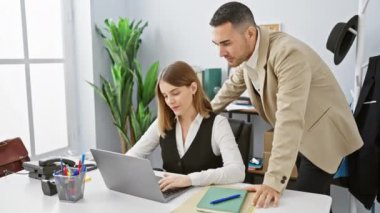 Parlak bir ofiste çalışan bir adam ve kadın laptopta iş tartışıyorlar..