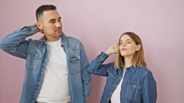 Kendine güvenen, kot gömlekli çekici bir çift pembe izole edilmiş arka planda poz veriyor, moda saçlara dokunuyor. Güzel gülümseyen yüzler birlikte neşe saçan aşk.