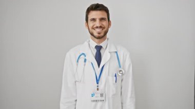Yakışıklı İspanyol genç adam, neşe ve güven saçıyor, mükemmel gülüşünü sergiliyor, steteskop takıyor. Soğuk beyaz bir arka planda izole edilmiş neşeli bir doktorun portresi.