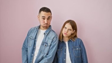 Kot gömlek giyen güzel bir çift komik bir pofuduk ifade takınıyorlar. Birlikte, izole pembe bir arka planda duruyorlar, yanakları şişiyor ve komik suratlar yapıyorlar..