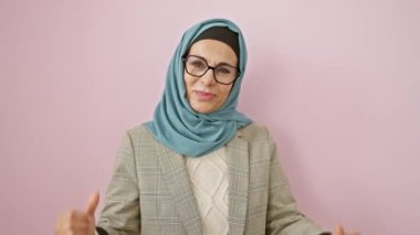 Orta yaşlı, tesettürlü İspanyol kadın kendine güveniyor. Aşırı neşeli ve gururlu. Pembe arka planda soyutlanmış.