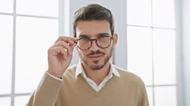 Neşeli, genç İspanyol bir adam bardakları iyi aydınlatılmış, modern bir ofise yerleştiriyor. Kendine güveni ve profesyonelliği var..