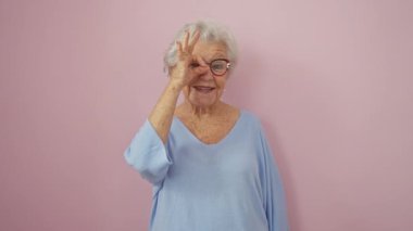 Neşeli, son sınıf öğrencisi bir işaret çakıyor, parmaklarından röntgenliyor. Gri saçlı, gözlük takan güzel, izole edilmiş pembe arka planda pozitif ışıldıyor..