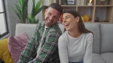 Modern bir oturma odasında rahat bir kanepede gevşeyen gülen İspanyol çift.