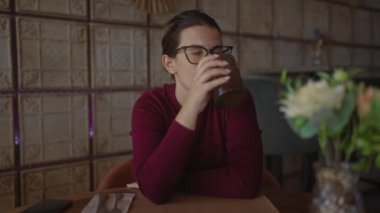Modern bir kafede içen düşünceli bir İspanyol kadın sıradan bir yemek deneyimini yakalar..