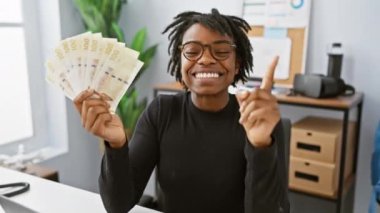 Ofiste garip fikirleri olan neşeli, genç siyahi bir kadın Danimarka kronu banknotunu şakaya vuruyor, soru soran bir yüzü var.!