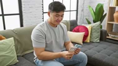 Genç bir Asyalı evdeki modern bir salonda oturarak Hong Kong doları sayıyor..