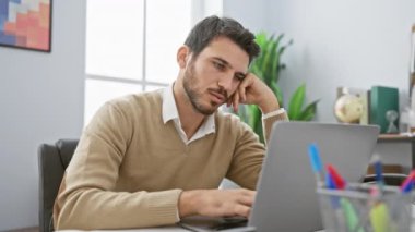 Modern bir ofis ortamında dizüstü bilgisayarla çalışırken esneyen yakışıklı bir İspanyol..