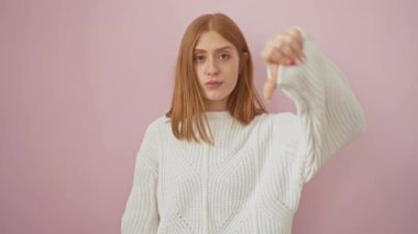 Hırkalı kızgın kızıl saçlı kadın, pembe arka planda olumsuz jestler yapıyor.