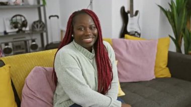 Kırmızı örgülü gülümseyen kadın rahat oturma odasında kanepede dinleniyor.