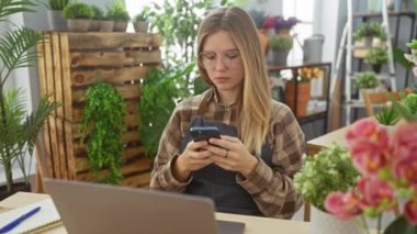 Çiçekçilik işini yürüten odaklı bir girişimci kadın içeride dizüstü bilgisayar ve akıllı telefon kullanıyor..