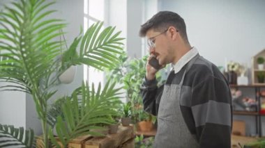 Çiçekçi dükkanında telefon görüşmesinde önlüklü genç adam çiçekçiyle ilgileniyor.