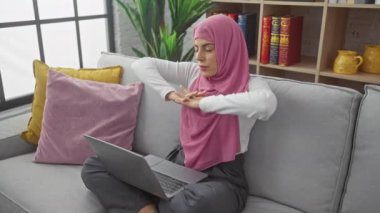 Konforlu bir oturma odasında dizüstü bilgisayarından çalışan tesettürlü bir kadın..