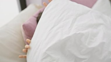 Neşeli, genç, İspanyol bir kadın rahat bir yatak odasında yastığı kucaklıyor. Rahatlık ve mutluluk saçıyor..