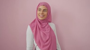 Kendine güvenen, tesettürlü genç İspanyol kadın doğal olarak gülümser. Rahatlamış profilinden kendine güvenir. Arap güzelliği, dışlanmış pembe bir duvara karşı anlamlı duruş..