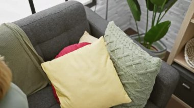 Rahat yetişkin bir kadın rahat bir oturma odasında akıllı telefonuyla kanepede uzanıyor.