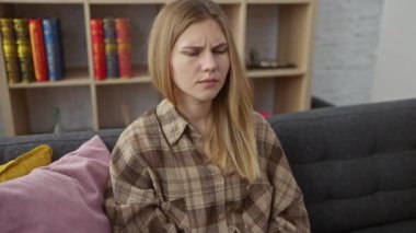 Şaşkınlık içindeki kuşkucu sarışın güzellik, iç kanepede oturan genç kadın, ağzı açık alaycı bir şok, şaşkın bakışlar, evde yüzünü yutan genç kadın.