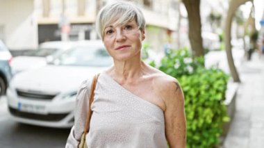 Kentin sokaklarında poz veren kısa gri saçlı, kendine güvenen, olgun bir kadın.