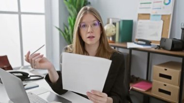 Ofiste bilgisayar ve belgelerle çalışan odaklı beyaz kadın.