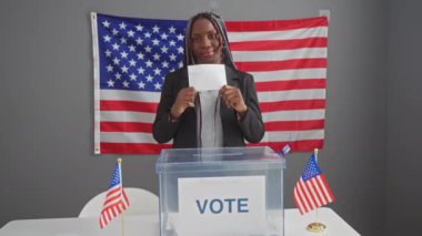 Örgü örgülü Afrikalı Amerikalı kadın içeride bayrak altında oy veriyor.