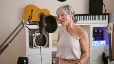 Olgun bir kadın bir müzik stüdyosunda mikrofon ve gitarlarla şarkı söylüyor, performans, eğlence ve tutku sergiliyor..