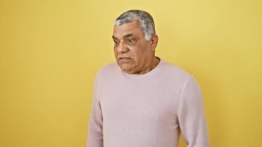 Alaycı şüpheci, orta yaşlı, beyaz saçlı, kafası karışmış, ağzı açık, şüpheci bakışları olan, izole edilmiş sarı duvarın önünde duran, züppe bir süveter giyen,