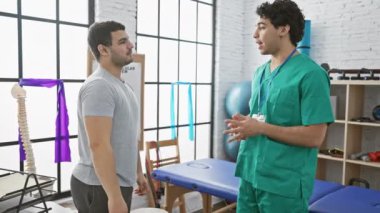 Erkek bir terapist, hastasına parlak bir fizyoterapi kliniğinde, sağlık hizmetleri ve rehabilitasyon hakkında bilgi verir..