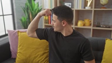 Kendine güvenen genç bir adam, rahat bir oturma odasında, rahat bir dekorla kaslarını kasarak gücünü gösterir..