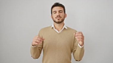 Işıldayan genç İspanyol adam meditasyon yapıyor, gözleri kapalı poz veriyor. Yoga yaparak, kazak giyerek ve ayakta durarak, izole edilmiş beyaz arka planda gevşemiş, ışık saçan sağlık ve huzur dolu bir hayat..