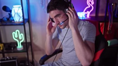 Gece renkli bir oyun odasında, neon ışıklarla aydınlatılmış, kulaklık takan odaklanmış bir adam..