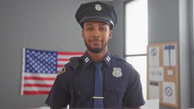 Gülümseyen bir Afro-Amerikan erkek polis memuru Amerikan bayrağıyla bir oy kullanma merkezinde 